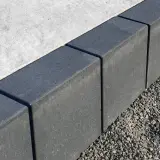 Szare obrzeża na podjazd, wykonane z kostki, oddzielają beton od żwiru.