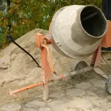 Betoniarka 120l czeka na cement. Obok piasek, łopata i kapelusz.