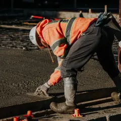 Robotnik w pomarańczowej kamizelce wygładza świeżą wylewkę. Zastanawiasz się, ile worków wylewki na 1m2 potrzeba?
