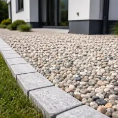 Podjazd z kamienia otoczony kamiennym obrzeżem i zieloną trawą przy nowoczesnym domu.