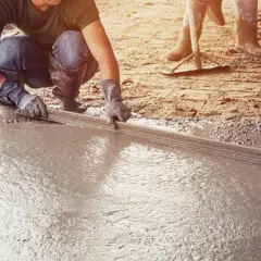 Pracownik wylewa betonową posadzkę w garażu za pomocą łaty.