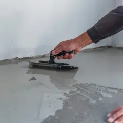 Ręka rozprowadza wylewkę samopoziomującą kielnią. Zastanawiasz się, ile na m2?