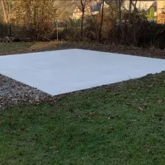 Nowa, jasna wylewka betonowa na gruncie, otoczona żwirem i trawą.