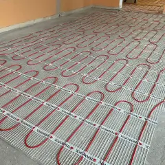Ułożone czerwone rurki ogrzewania podłogowego na siatce.