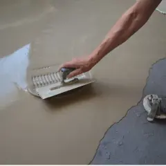 Ręka z kielnią rozprowadza masę samopoziomującą na podłodze.
