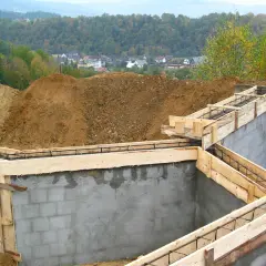 Fundament budowy z szalunkiem i zbrojeniem, w tle domy i las.