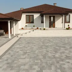 Nowoczesny podjazd z szarej kostki brukowej, idealnie komponuje się z białym domem i brązowym dachem.