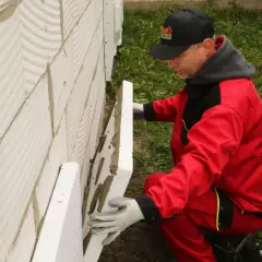 Budowlaniec w czerwonym stroju montuje płyty styropianowe. Pytanie brzmi: jaka grubość styropianu na fundament będzie najlepsza?