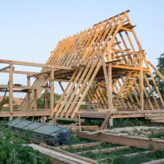 Drewniana konstrukcja domku letniskowego w budowie. Widać szkielet dachu i ścian, a także elementy, które mogą stanowić jaki fundament pod domek letniskowy drewniany.