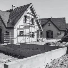 Budowa domów w toku. Scena pokazuje postęp prac, jak przenieść pozwolenie na budowę, gdy domy są w stanie surowym, z rusztowaniami i koparką.