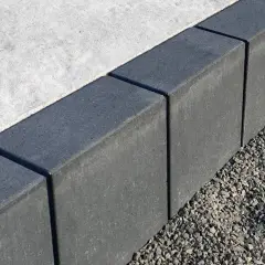 Szare obrzeża na podjazd, wykonane z kostki, oddzielają beton od żwiru.