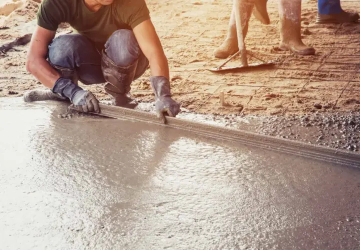Pracownik wylewa betonową posadzkę w garażu za pomocą łaty.