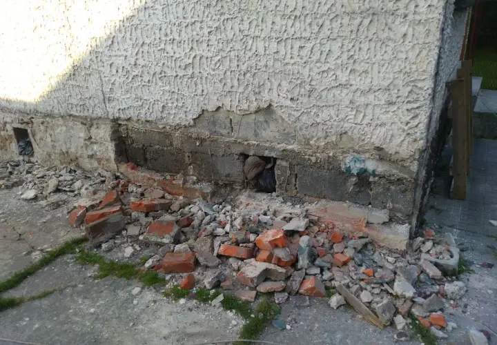 Odkopany fragment ściany z widocznymi uszkodzeniami, gruz i cegły. Rozpoczęcie prac, jak wzmocnić stare fundamenty z kamienia.