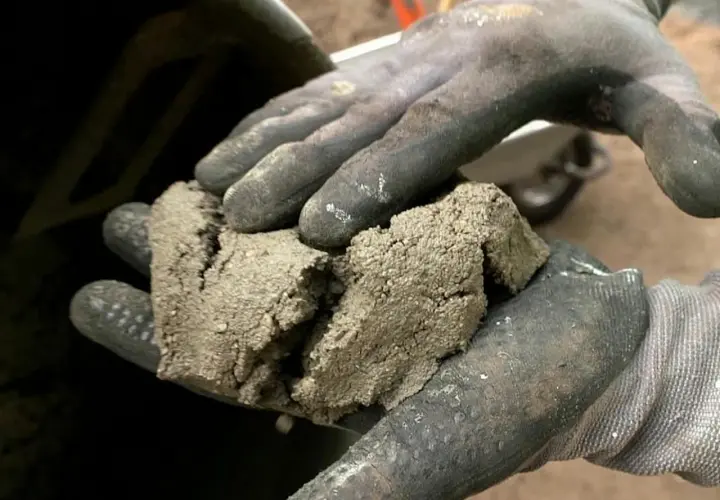 Rękawice robocze trzymają grudki zaschniętego betonu, co jest pierwszym krokiem w procesie, jak wyczyścić betoniarkę.