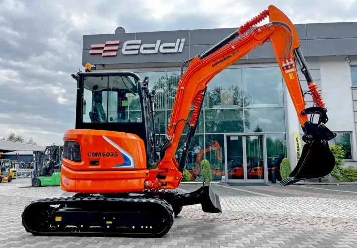 Pomarańczowa koparka gąsienicowa CDM 6035 przed budynkiem z logo Eddi.