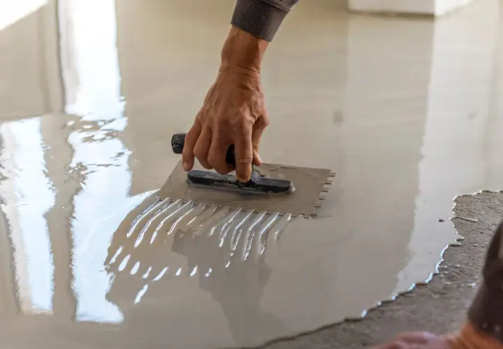 Dłoń zacierająca świeżą wylewkę samopoziomującą na podłodze. Precyzyjne rozprowadzenie materiału określa, ile wylewki samopoziomującej na m2 zostanie zużyte.