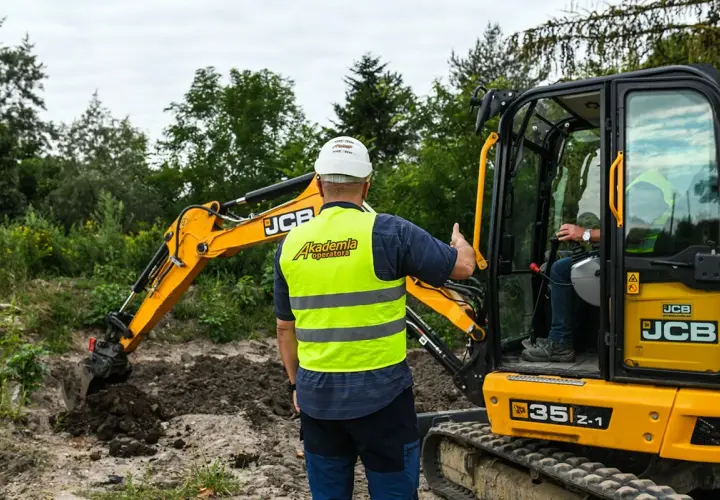 Instruktor pokazuje, jak szybko można ukończyć kurs na koparkę. Operator w kamizelce "Akademia Operatora" uczy się obsługi maszyny JCB.