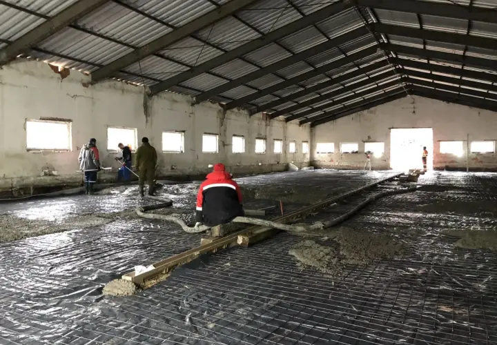 Pracownicy wylewają beton na zbrojenie wewnątrz hali.