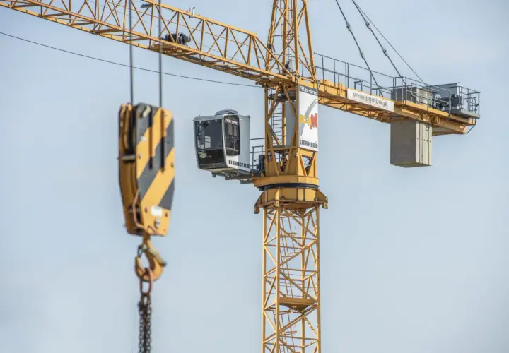 Żółty dźwig budowlany z kabiną operatora i hakiem. Widać fragmenty konstrukcji i logo Liebherr.