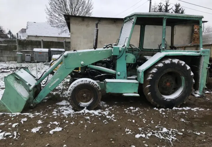 Zielona ładowarka Ostrówek KTO-162 stoi na błotnistym podwórku, pokryta śniegiem.
