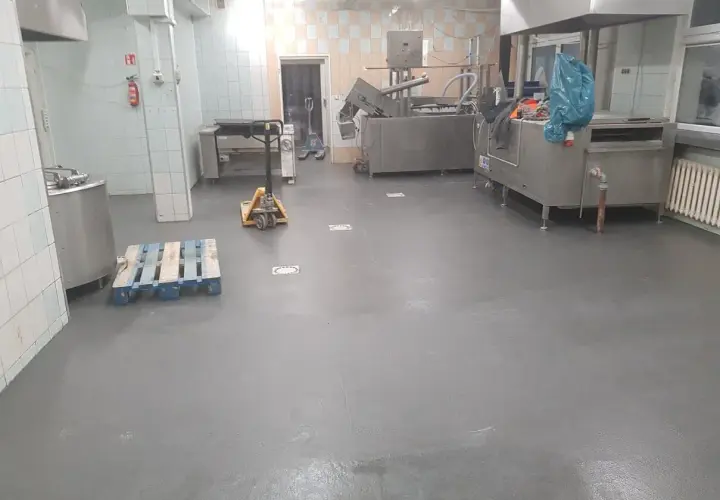 Nowa, szara wylewka betonowa w kuchni przemysłowej schnie, czekając na dalsze prace.