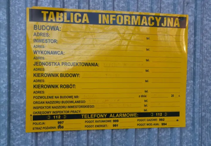 Tablica informacyjna na budowie. Widać pola na dane inwestora, kierownika budowy, numer pozwolenia na budowę i telefony alarmowe. Ważne jest pozwolenie na budowę, by wszystko było legalne.
