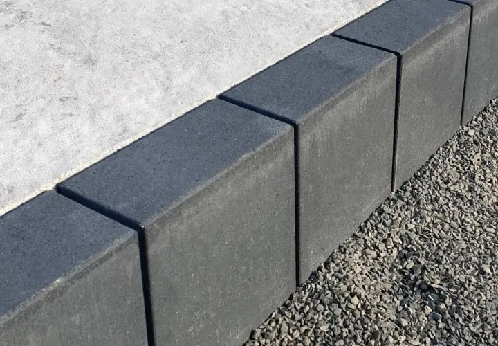 Szare obrzeża na podjazd, wykonane z kostki, oddzielają beton od żwiru.