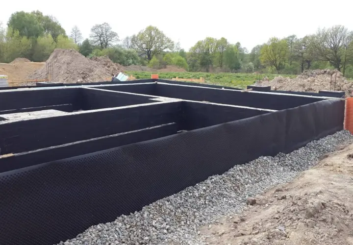 Fundament domu w budowie, z czarną izolacją i otoczakami.