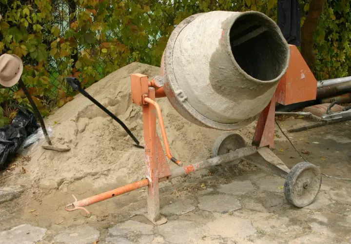 Betoniarka 120l czeka na cement. Obok piasek, łopata i kapelusz.