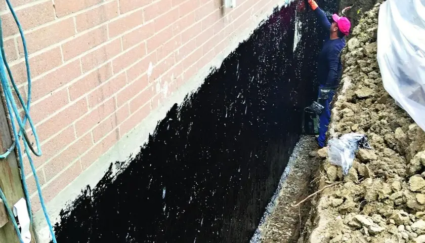 Pracownik nakłada czarną hydroizolację na ścianę fundamentową.