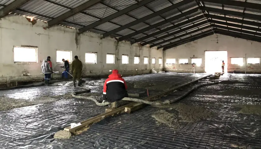 Pracownicy wylewają beton na zbrojenie wewnątrz hali.
