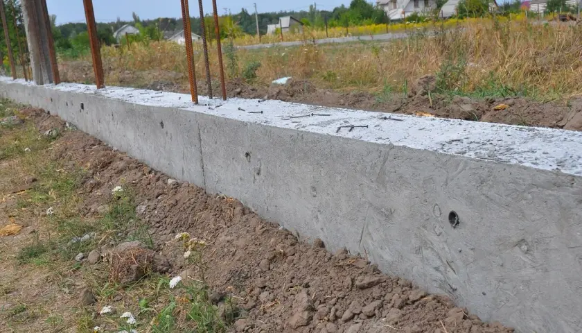 Nowy betonowy fundament z wystającymi prętami zbrojeniowymi, gotowy do połączenia ze starym fundamentem.