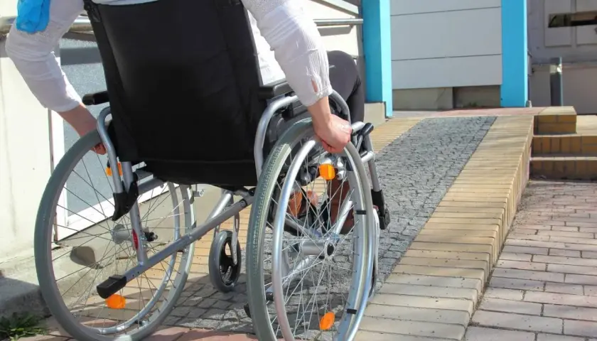 Osoba na wózku inwalidzkim wjeżdża na podjazd, pokazując, jak zrobić podjazd dla niepełnosprawnych.