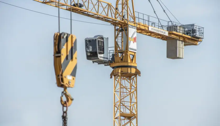 Żółty dźwig budowlany z kabiną operatora i hakiem. Widać fragmenty konstrukcji i logo Liebherr.