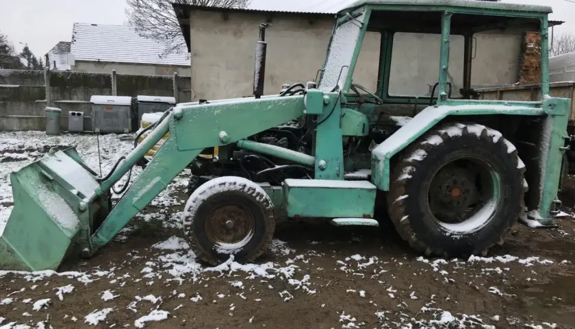 Zielona ładowarka Ostrówek KTO-162 stoi na błotnistym podwórku, pokryta śniegiem.