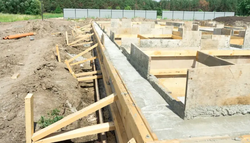 Budowa fundamentów pod dom szkieletowy. Betonowe ławy i szalunki drewniane tworzą solidną podstawę.