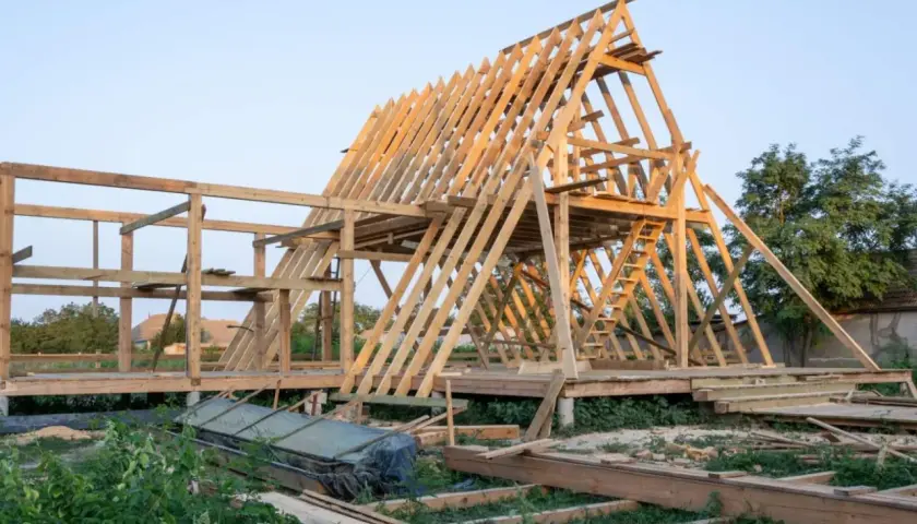 Drewniana konstrukcja domku letniskowego w budowie. Widać szkielet dachu i ścian, a także elementy, które mogą stanowić jaki fundament pod domek letniskowy drewniany.