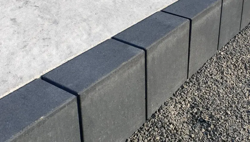 Szare obrzeża na podjazd, wykonane z kostki, oddzielają beton od żwiru.