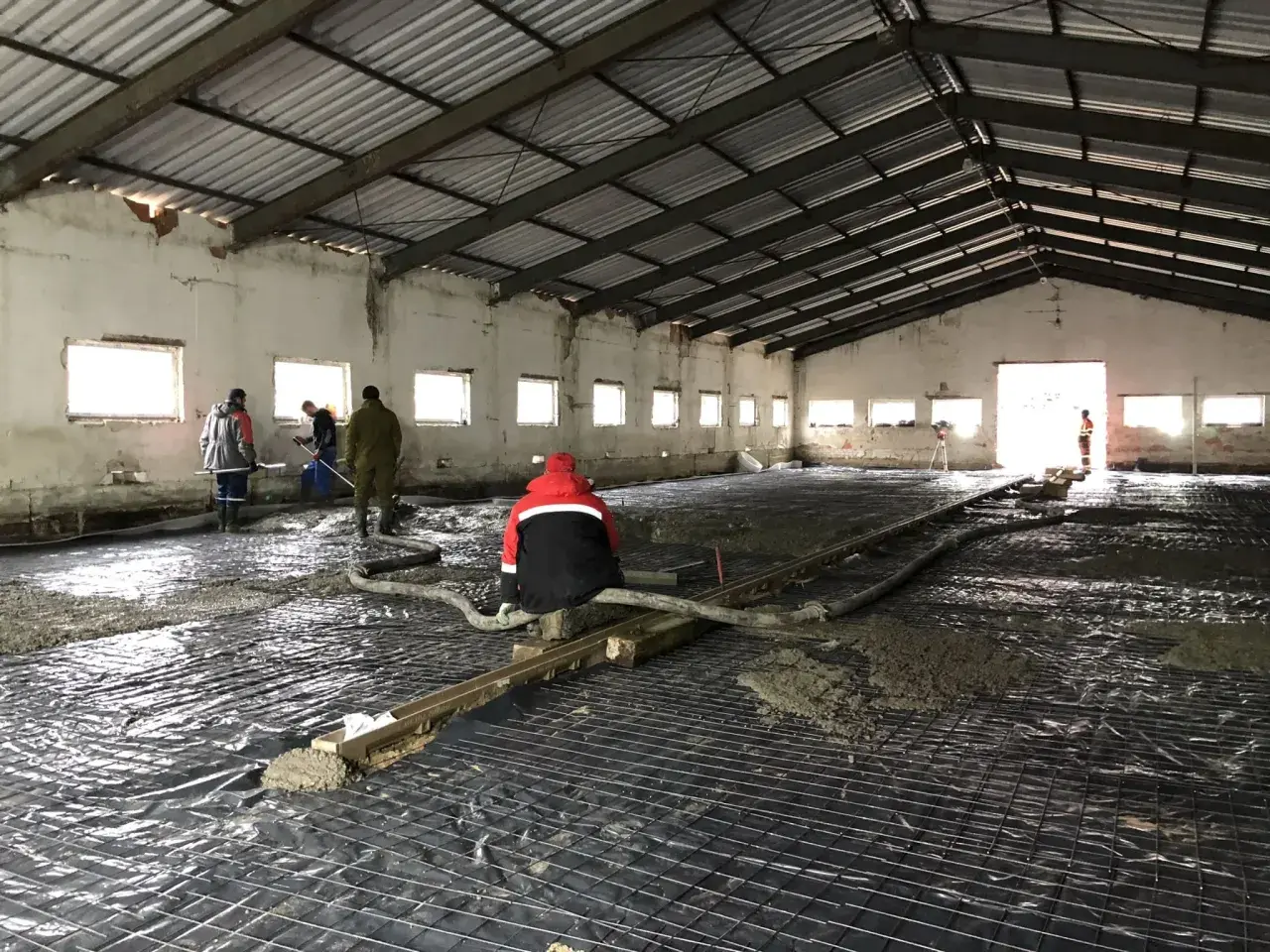 Pracownicy wylewają beton na zbrojenie wewnątrz hali.