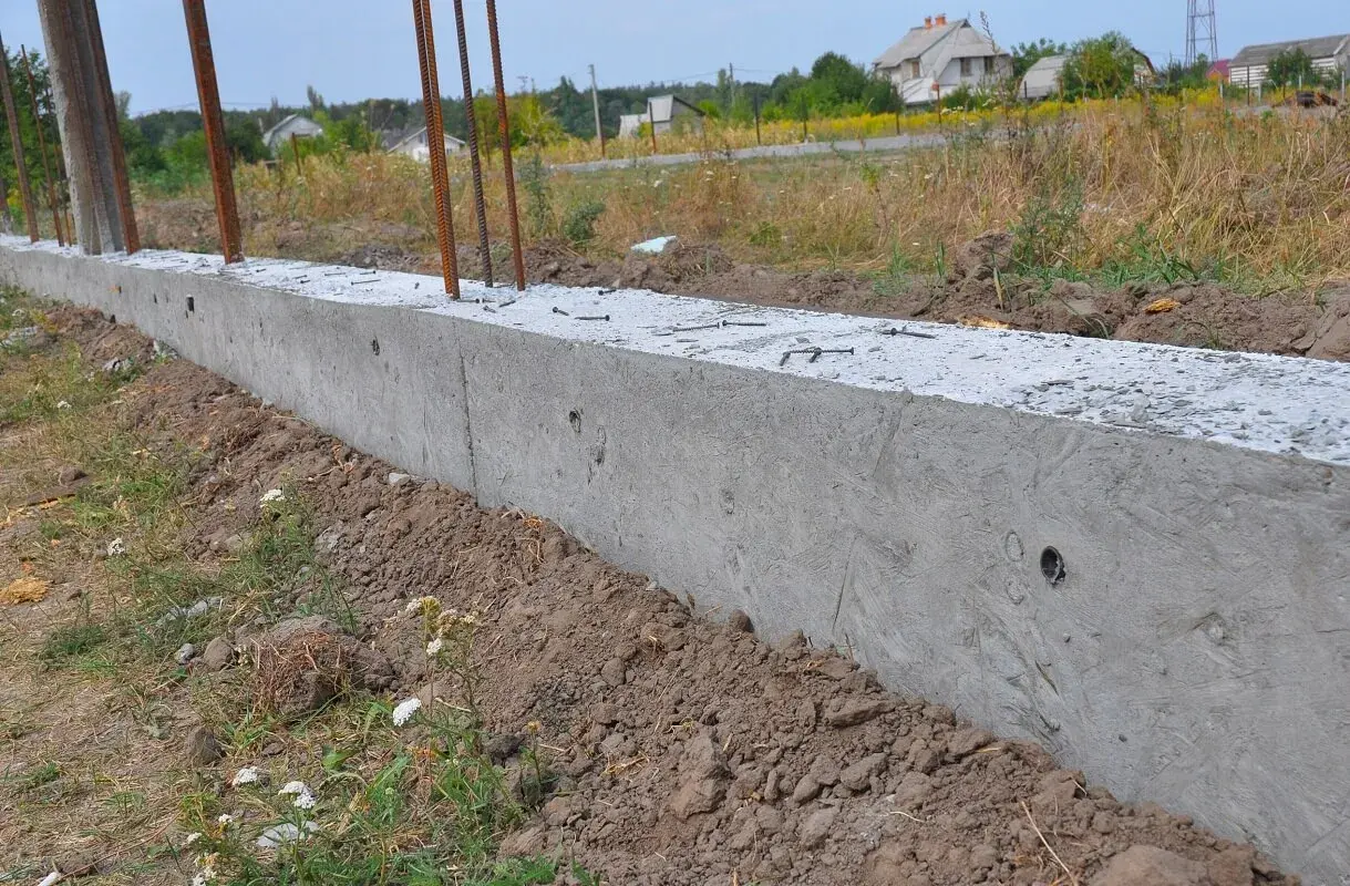 Nowy betonowy fundament z wystającymi prętami zbrojeniowymi, gotowy do połączenia ze starym fundamentem.