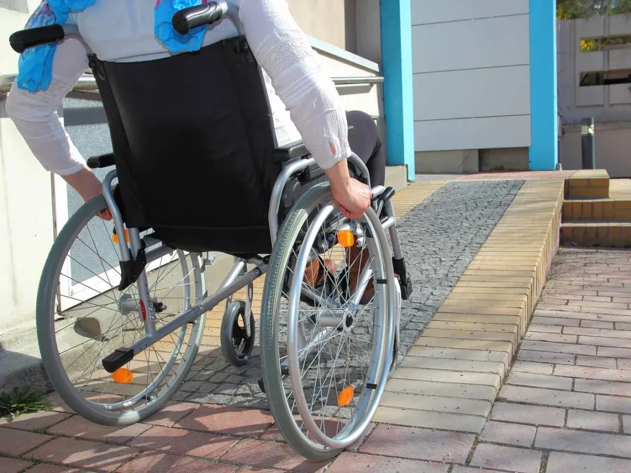 Osoba na wózku inwalidzkim wjeżdża na podjazd, pokazując, jak zrobić podjazd dla niepełnosprawnych.