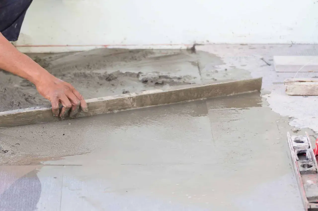 Ręka pracownika wyrównuje świeżą wylewkę betonową. Zastanawiasz się, ile waży wylewka betonowa?