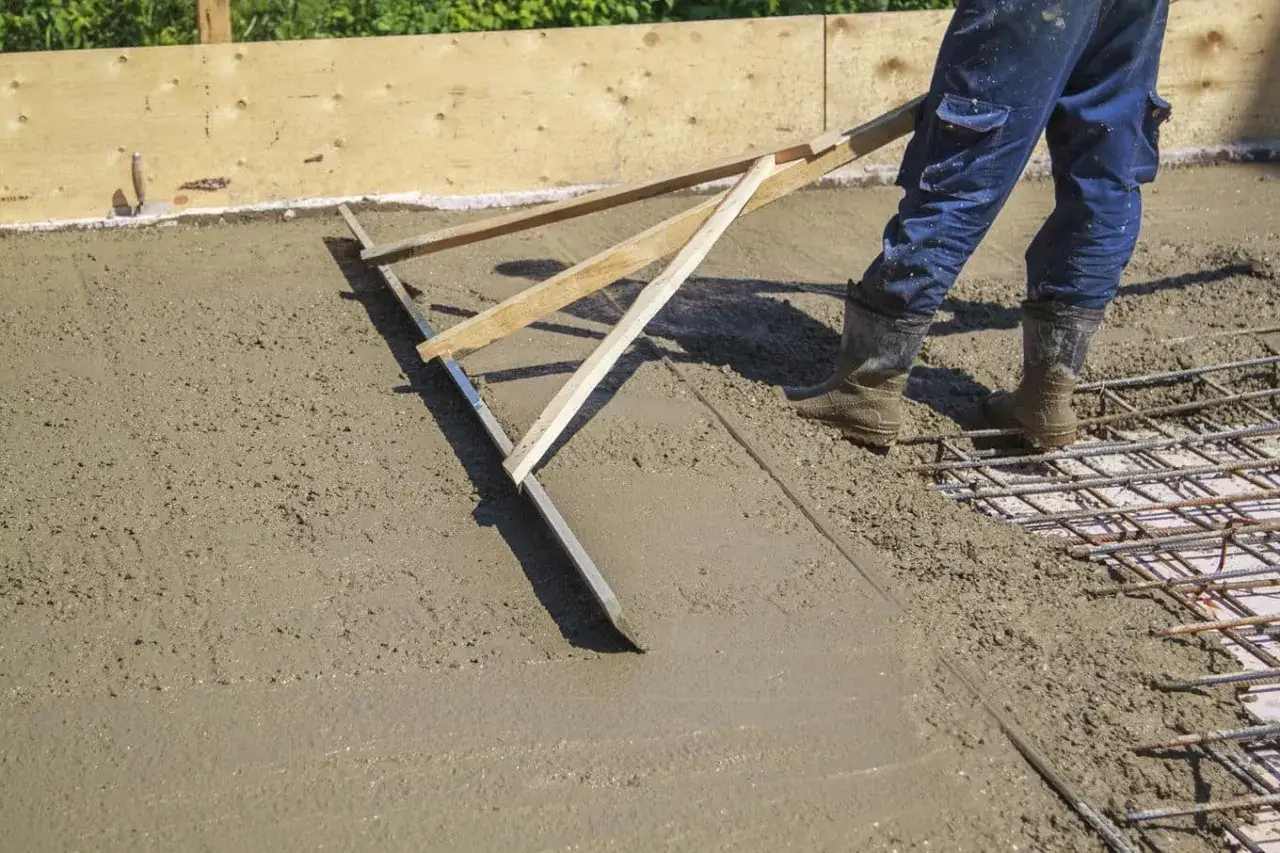 Pracownik wyrównuje świeżą wylewkę betonową za pomocą łaty. Dowiedz się, jak zrobić wylewkę betonową.