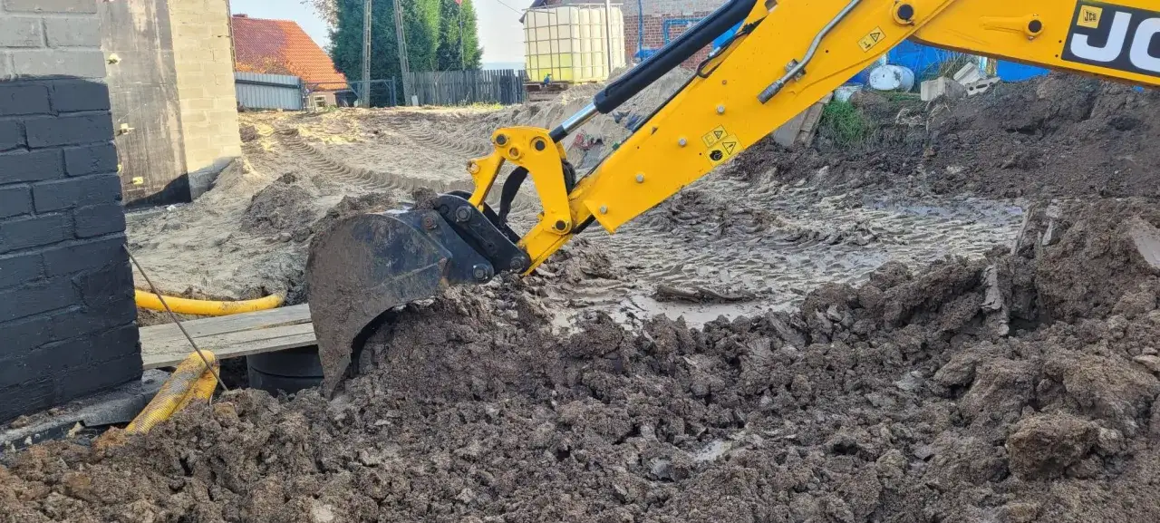 Żółta koparka JCB pracuje na budowie, kopiąc ziemię. Zastanawiasz się, ile kosztuje koparka?