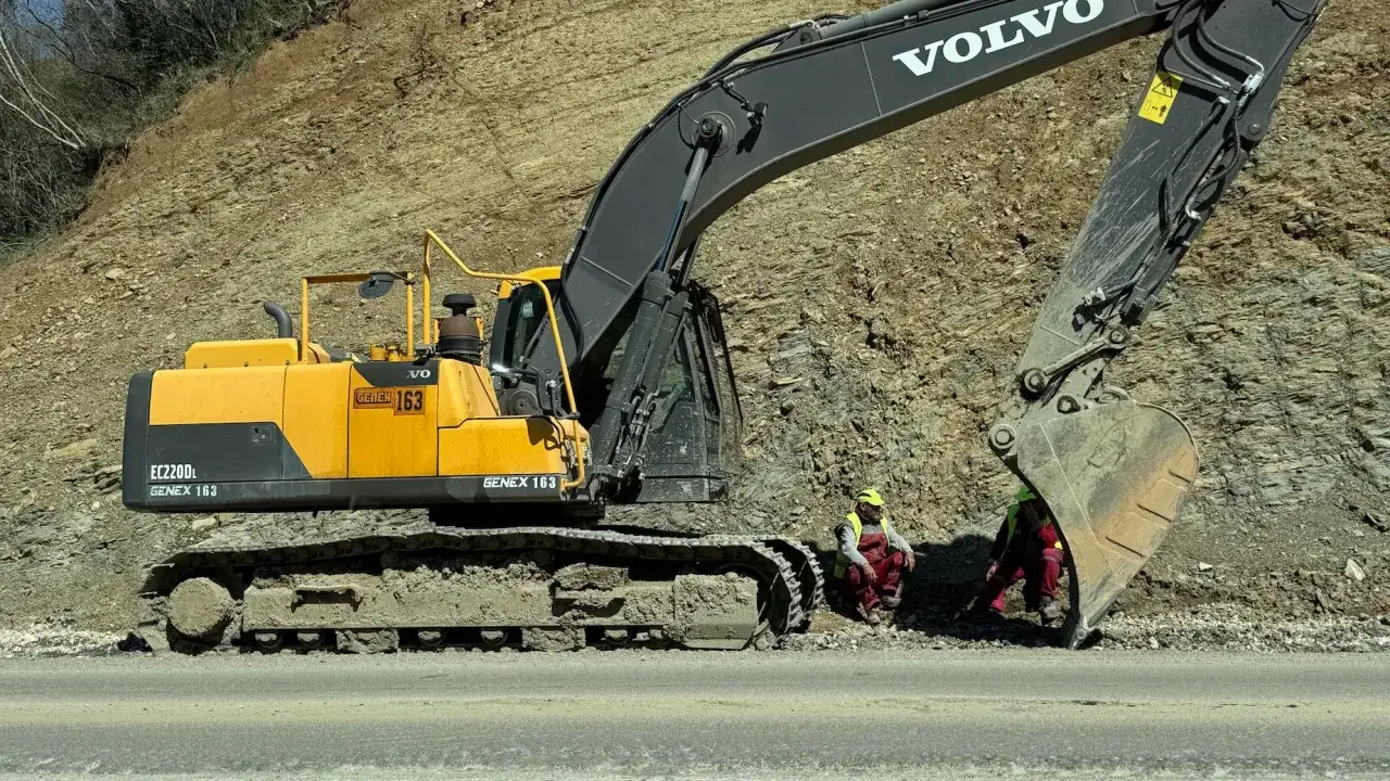 Żółta koparka Volvo EC220DL z numerem GENEX 163 pracuje przy osuwisku. Dwóch pracowników w kamizelkach odblaskowych odpoczywa. Zastanawiasz się, ile kosztuje koparka?