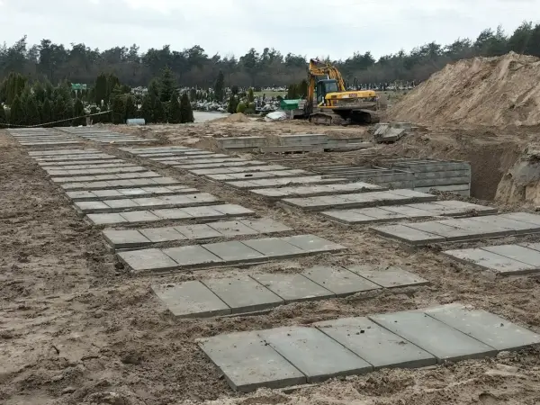 Przygotowanie terenu na cmentarzu, gdzie układane są płyty betonowe. Zastanawiasz się, ile kosztuje fundament pod pomnik? Tu widać początek prac.