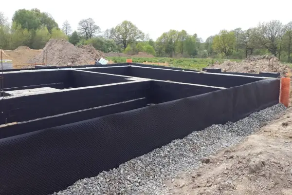 Fundament domu w budowie, z czarną izolacją i otoczakami.